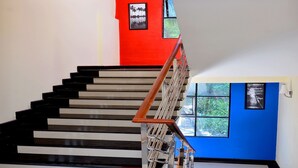 A staircase with black and white steps, a wooden handrail, and a red wall with a framed picture. - French Avenue (Mahe)