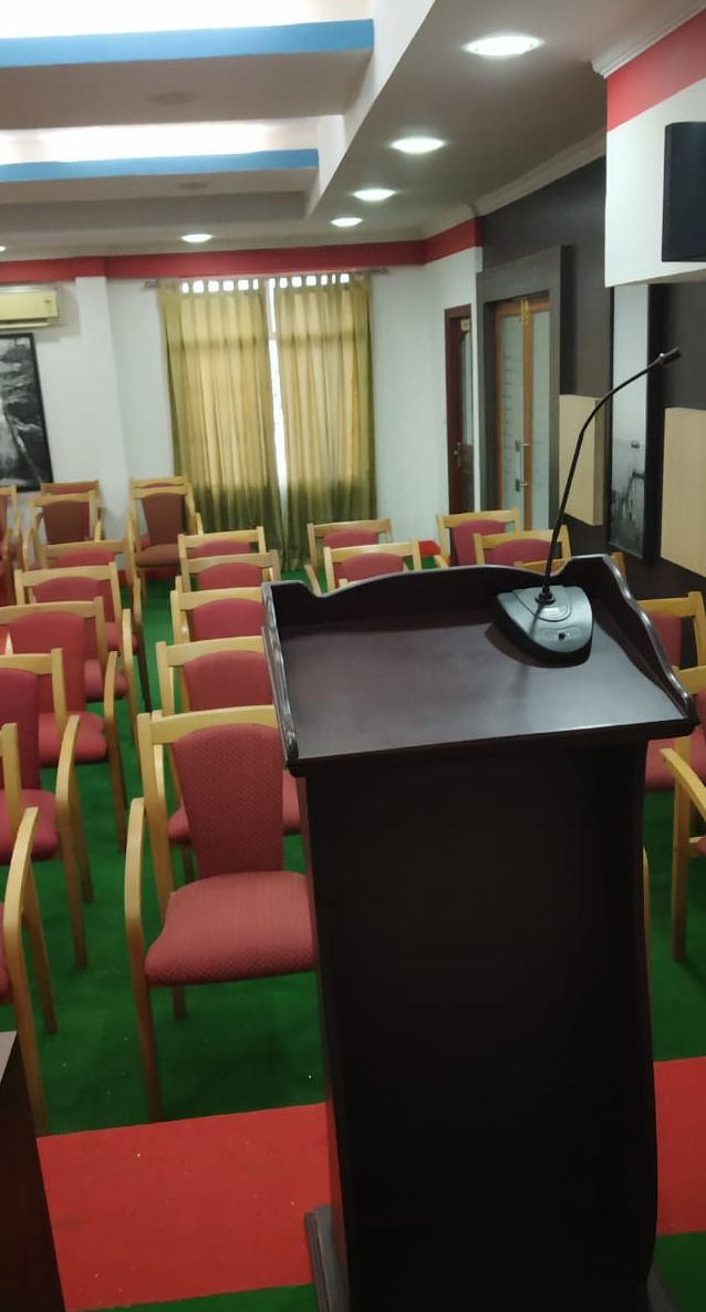 Un salón de conferencias con filas de sillas, un atril y alfombra verde.