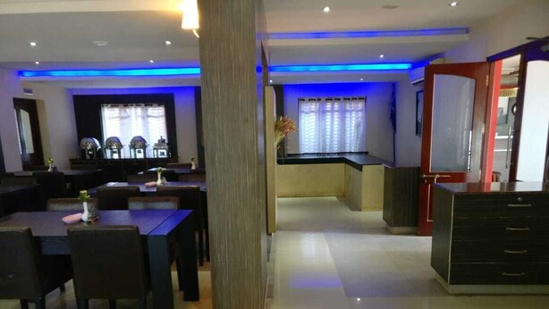 A modern hotel lobby with a dining area, a reception desk, and a kitchen in the background. - French Avenue (Mahe)
