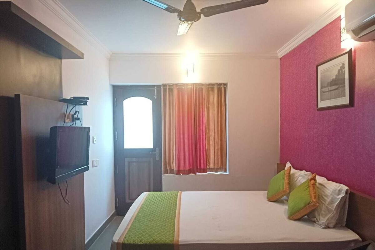 Un dormitorio con cama, televisión montada en la pared, ventana con cortinas y ventilador de techo.