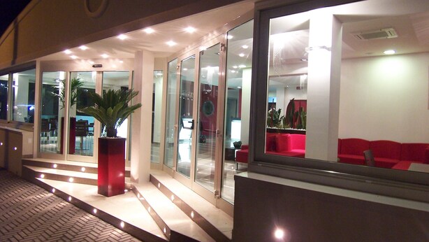 Un bâtiment moderne avec des portes et des fenêtres en verre, un espace détente rouge et une plante en pot.