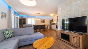 Een moderne woonkamer met een grijze bank, een houten salontafel en een grote flatscreen-tv op een houten kast.