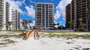 Un hotel fronte spiaggia con una torre centrale, palme e un vialetto sabbioso.