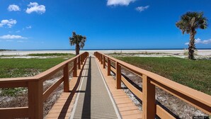 Una passerella di legno che conduce a una spiaggia, con palme e un cielo azzurro limpido.