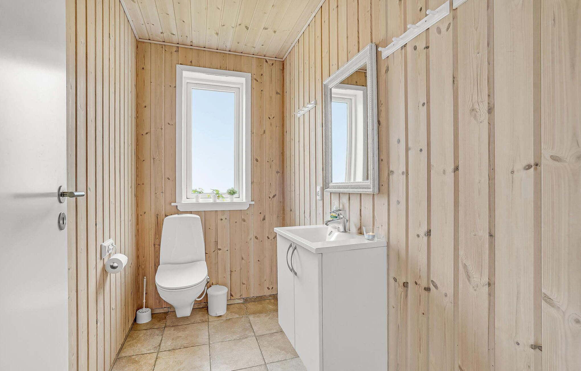 A small, wooden-paneled bathroom with a toilet, sink, and mirror.