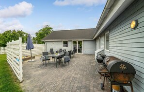 Un patio con una parrilla, mobiliario exterior y una cerca blanca.