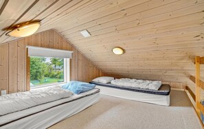 Un dormitorio acogedor en el ático con dos camas, un ventanal grande y techo inclinado.