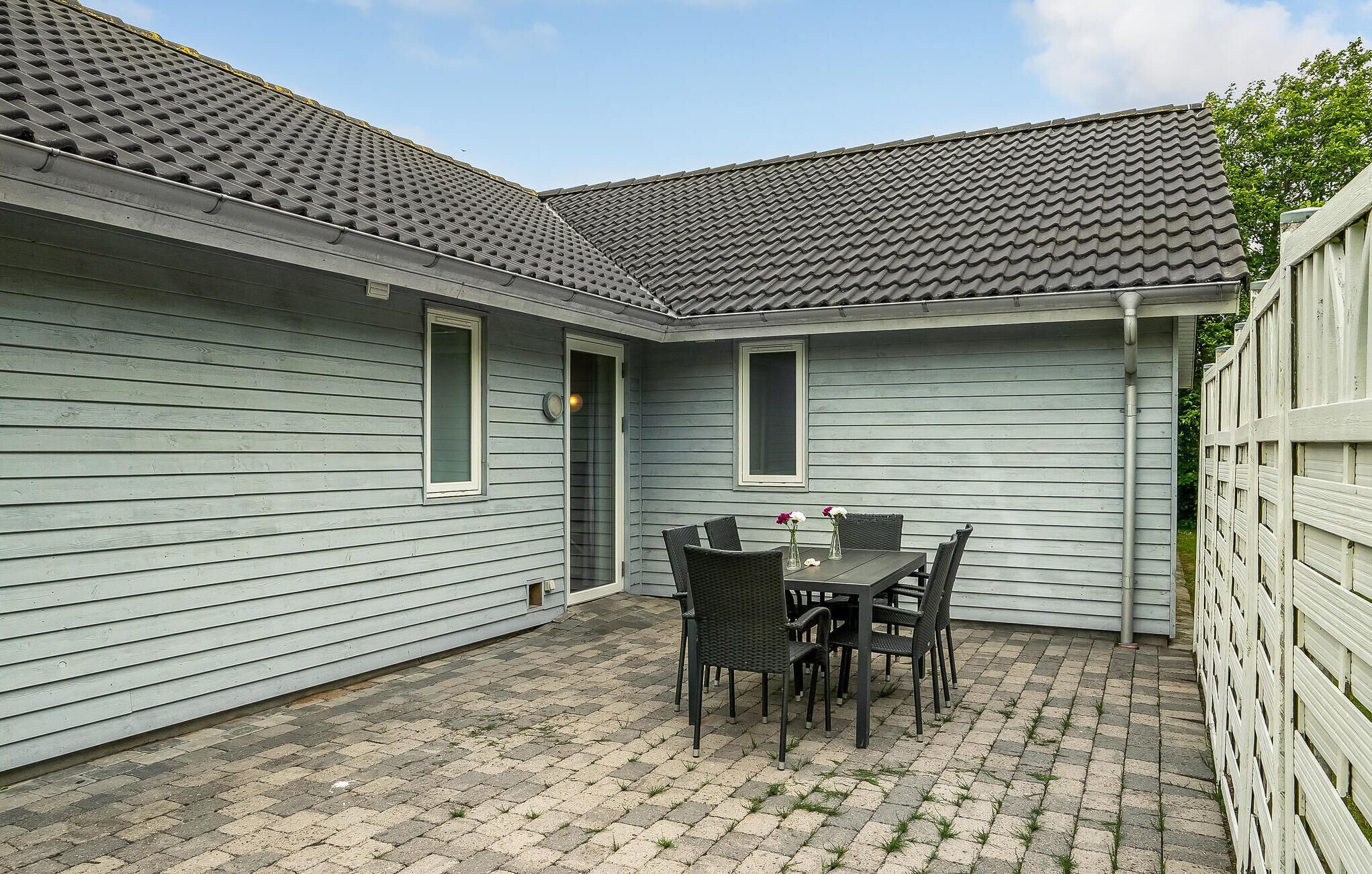 A patio area with a table and chairs, a small window, and a white fence.