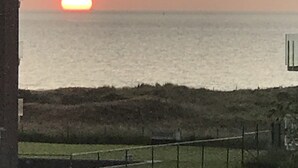 A sunset over the ocean with a grassy area and a fence in the foreground.