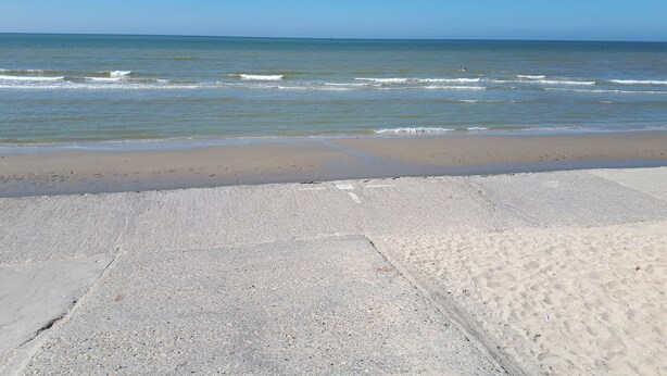 A beach with a concrete walkway leading to the water.