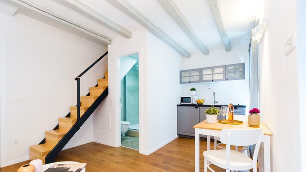A modern kitchen with a wooden staircase, a dining area with a table and chairs, and a view of the adjacent bathroom. - Cozy Montalbano Studios by Irundo (Rovinj)