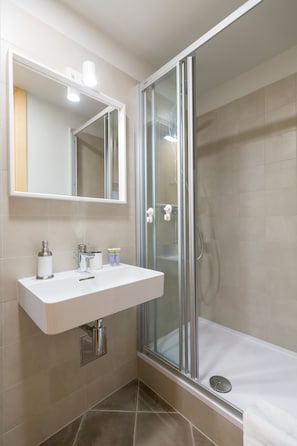 A modern bathroom with a glass-enclosed shower, a white sink, and a mirror above it. - Cozy Montalbano Studios by Irundo (Rovinj)