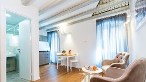 A modern living room with a wooden floor, a round coffee table, two armchairs, a dining table with chairs, and a kitchen in the background. - Cozy Montalbano Studios by Irundo (Rovinj)