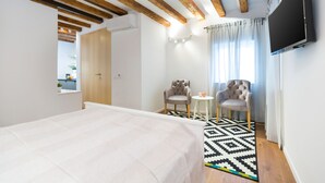A bedroom with a bed, a TV, two chairs, a small table, and a patterned rug. - Cozy Montalbano Studios by Irundo (Rovinj)