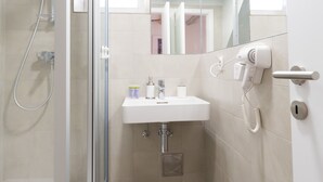 A modern bathroom with a glass shower enclosure, a white sink, and a hairdryer mounted on the wall. - Cozy Montalbano Studios by Irundo (Rovinj)
