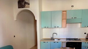 Ett kompakt kök med turkosa skåp, ett matbord med stolar och en soffa.