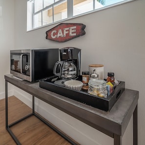Eine Küchenzeile mit Kaffeemaschine, Mikrowelle und einer Kaffeestation, ausgestattet mit verschiedenen Behältern und einem Glas gemahlener Kaffeebohnen.
