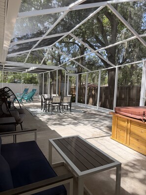 A covered patio with a table and chairs, a wooden bench, and a hot tub.