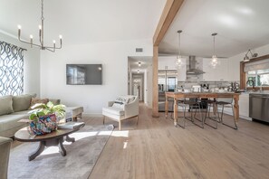 Una sala de estar moderna con sofá, mesa de centro y comedor, con una cocina al fondo.