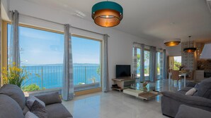 A spacious living room with a large window overlooking a scenic view, a flat-screen TV, and modern furniture. - Holiday home Villetta Belveder (Baska Voda)