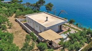 A modern house with a flat roof, surrounded by greenery and overlooking a clear blue sea. - Holiday home Villetta Belveder (Baska Voda)