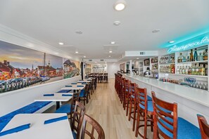 Un restaurante con una barra larga, sillas de madera y una zona de bar con un letrero de neón.