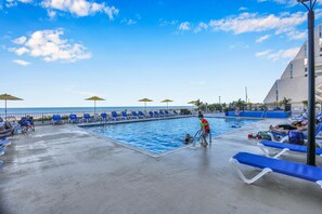 Un área de piscina con sillones de descanso y sombrillas, piscina y vista al océano.