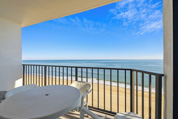 A balcony with a table and chairs overlooking a beach.