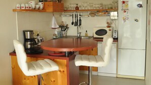 A compact kitchen with wooden cabinets, a central island with stools, a white refrigerator, and basic appliances. - La Rochelle T2 35m2 Avec Terrasse Dans Résidence de Standing (La Rochelle)