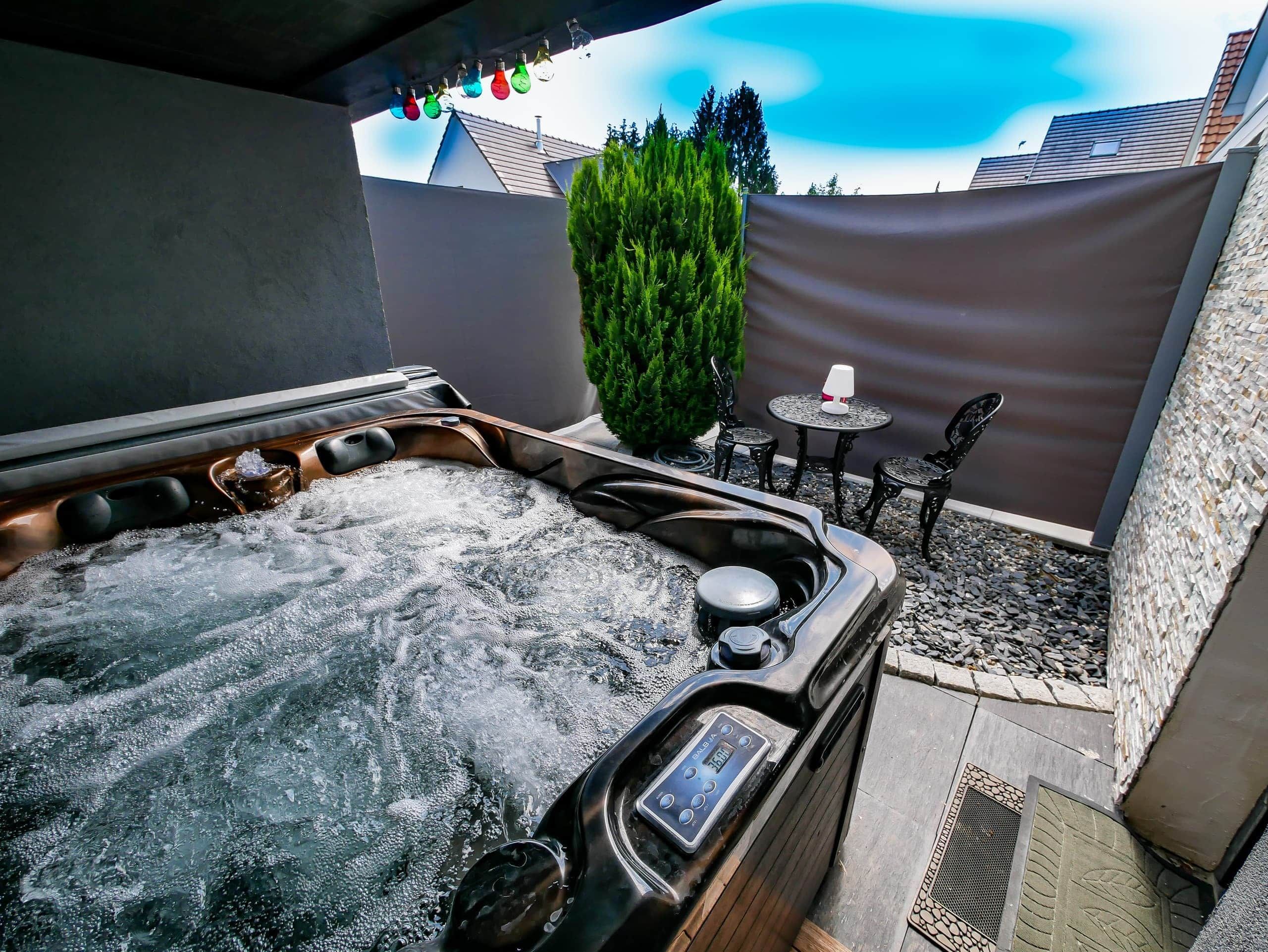 A hot tub with a control panel, surrounded by outdoor seating and a decorative hedge.