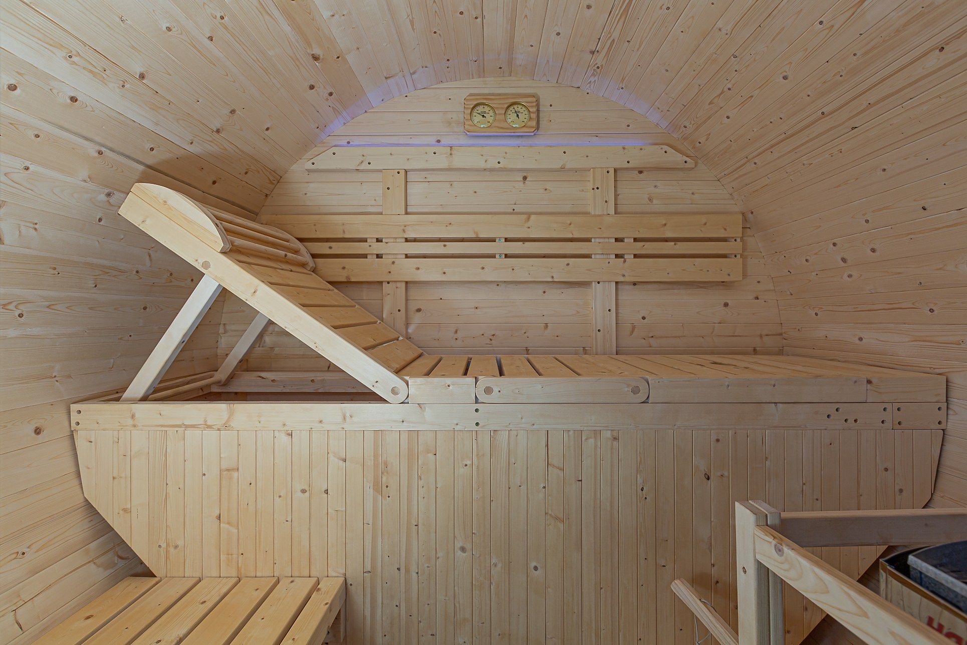 Una sauna amb parets i bancs de fusta, sostre inclinat i un rellotge.