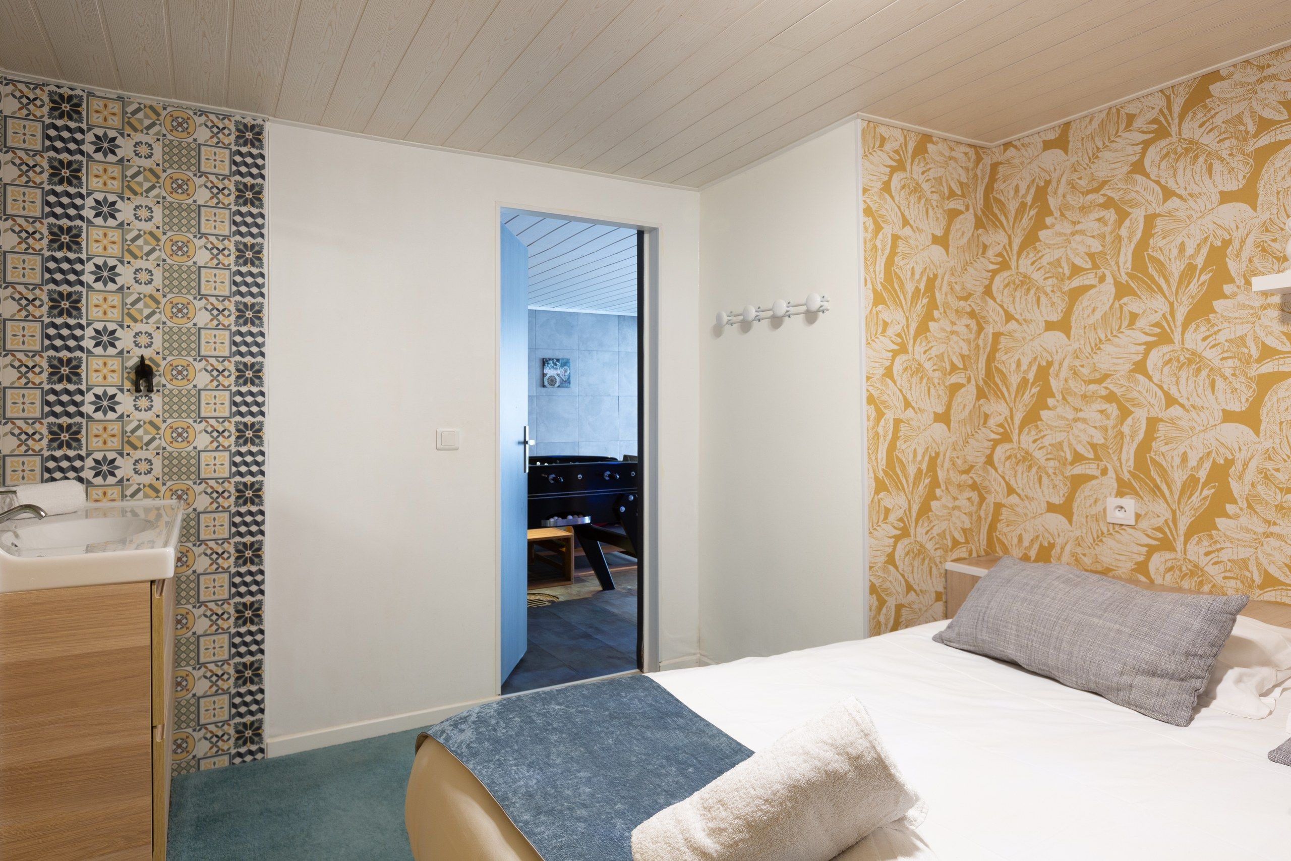 A bedroom with a bed, a bedside table, a sink, and a patterned wall.