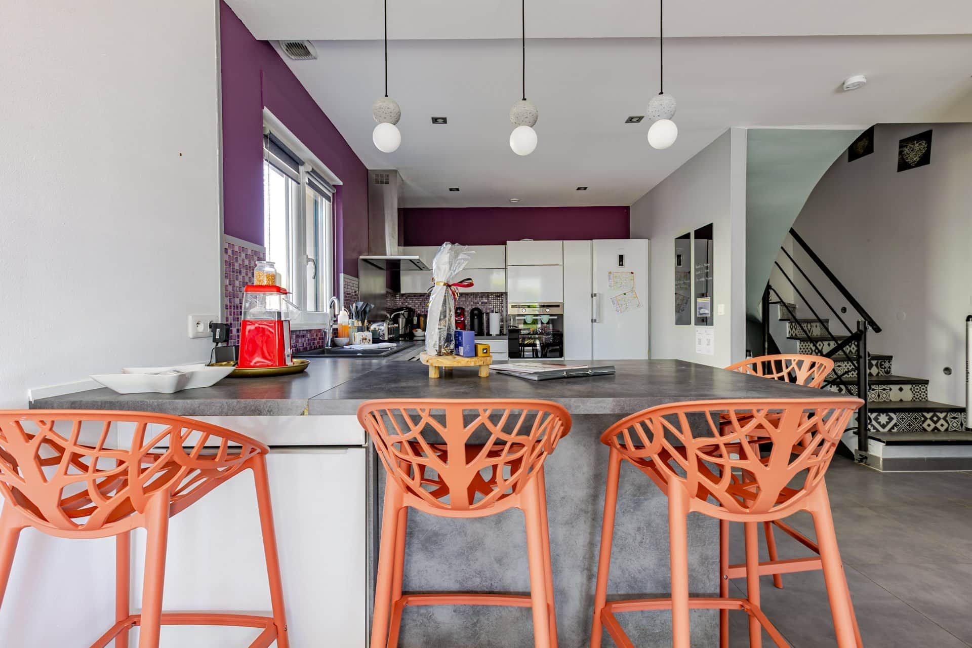 Une cuisine moderne dotée d’un îlot central, de tabourets de bar et d’un escalier menant à un niveau supérieur.