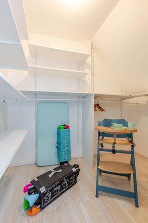 Un cuarto de almacenamiento con estantes, un contenedor azul, una silla de madera con una bandeja y un mueble negro con ruedas.