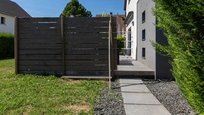 Um edifício moderno com cerca de madeira, caminho de concreto e jardim bem cuidado.