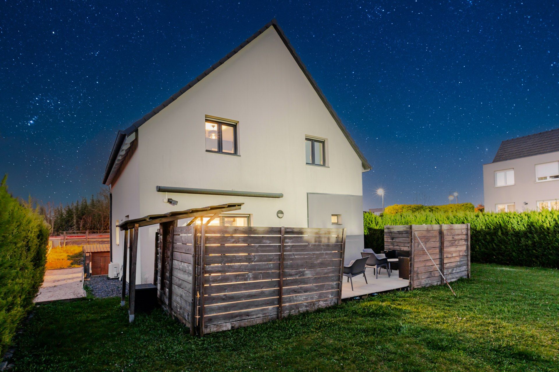 A two-story house with a sloped roof, a covered patio with outdoor furniture, and a well-maintained lawn.