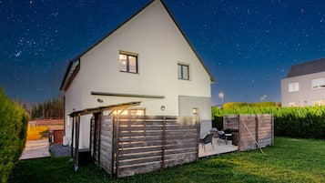 A two-story house with a sloped roof, a covered patio with outdoor furniture, and a well-maintained lawn.