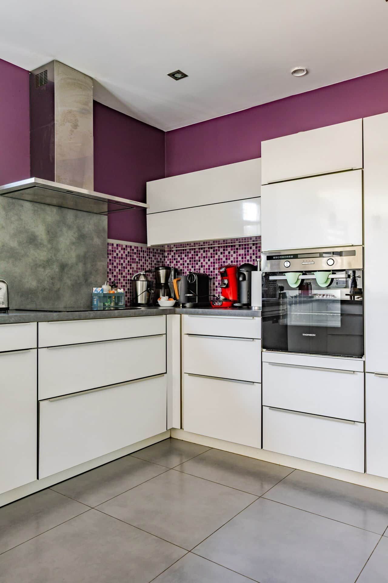 Eine moderne Küche mit weißen Schränken, einem eingebauten Backofen und einer violetten Spritzschutzwand.