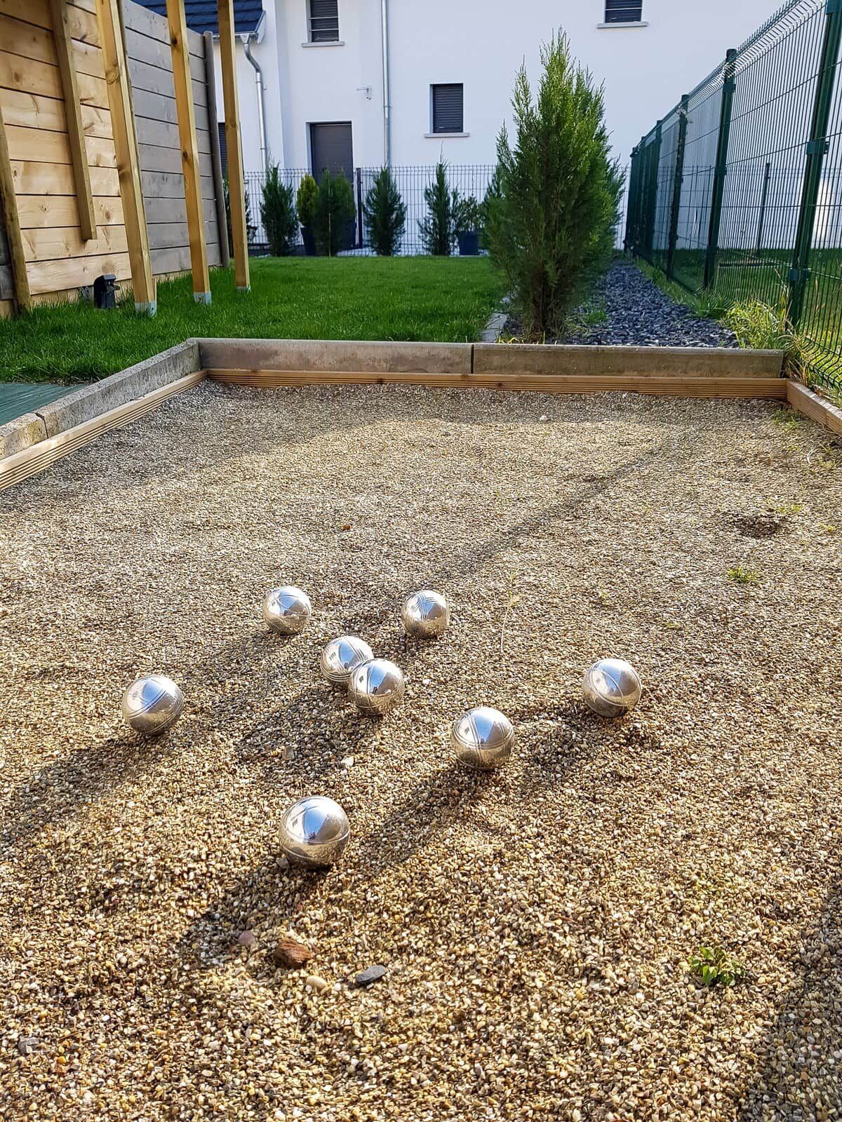 Un patio con suelo de grava y varias esferas metálicas.