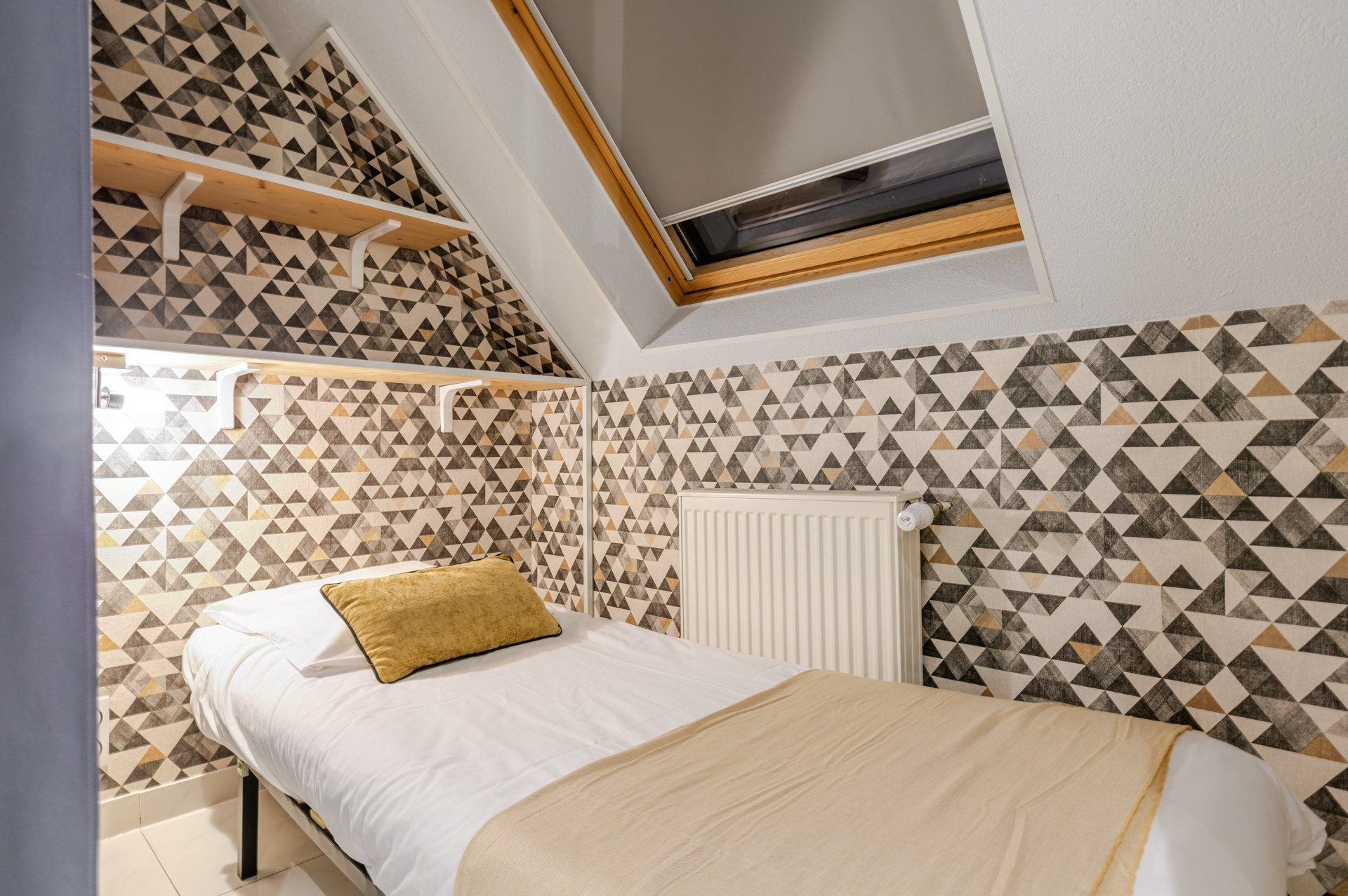 A bedroom with a bed, a radiator, and a geometric patterned wall.