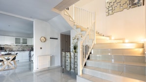 A modern kitchen with white cabinets, a dining table, and a staircase with a white railing. - Villa 180m² with private spa, barbecue, table football (Ittenheim)