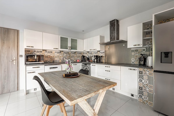 Een moderne keuken met witte kasten, een houten eettafel en betegelde spatwand met een patroon.