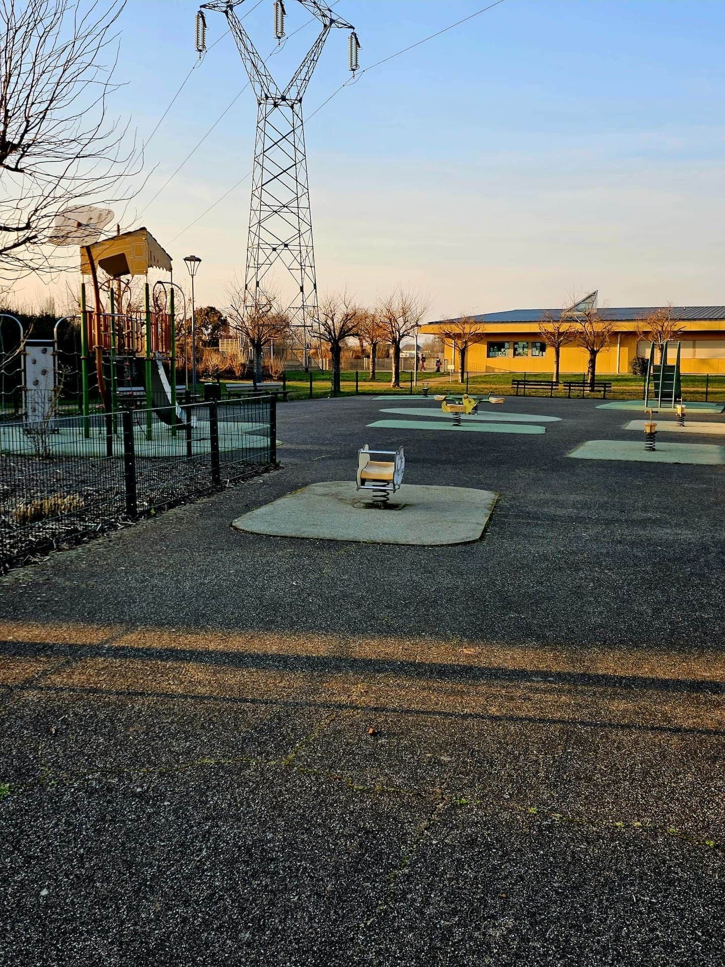 A playground with equipment, a fenced area, and a building in the background.