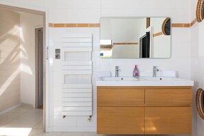Ein Badezimmer mit einem weißen Heizkörper, einem Holzwaschtisch, einem großen Spiegel und einem weißen Waschbecken.