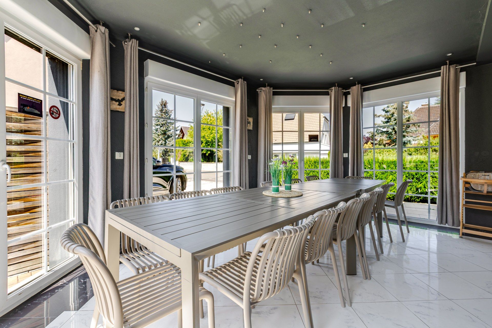 Un espace repas avec une longue table et des chaises, de grandes fenêtres et une vue sur la verdure environnante.