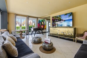 A hotel lobby with a sofa, a table, chairs, a television, and a painting. - Villa Ours – Private spa, games room, 15 guests (Ittenheim)