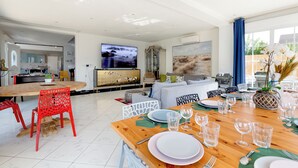 A modern living room with a dining area, a kitchen in the background, and a large TV on the wall. - Villa 200m² with private spa, barbecue, table football (Ittenheim)