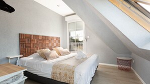 A bedroom with a herringbone-patterned headboard, a bed with white bedding, a wooden floor, a small red basket, and a window with blinds. - Villa 200m² with private spa, barbecue, table football (Ittenheim)