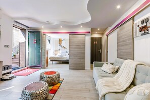 Ein modernes Wohnzimmer mit einer Couch, Hocker und einem Bett im Hintergrund.