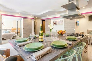 A modern kitchen with a dining area, equipped with green plates, wine glasses, and a bottle of champagne.